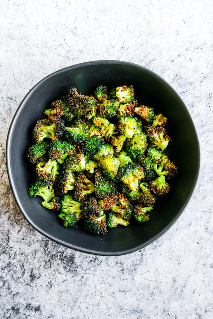 a black bowl of air fryer broccoli on a grey background