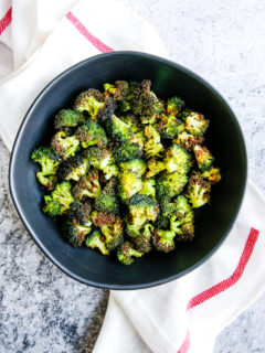 a bowl of air fryer broccoli in a black bowl on a red and white napkin