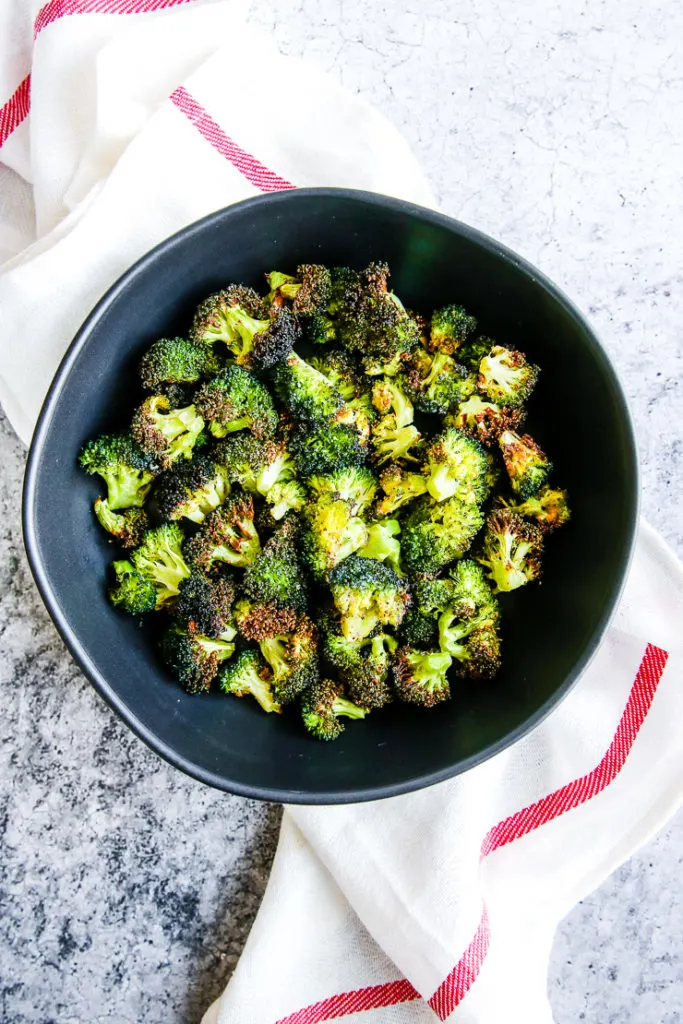 a bowl of air fryer broccoli in a black bowl on a red and white napkin