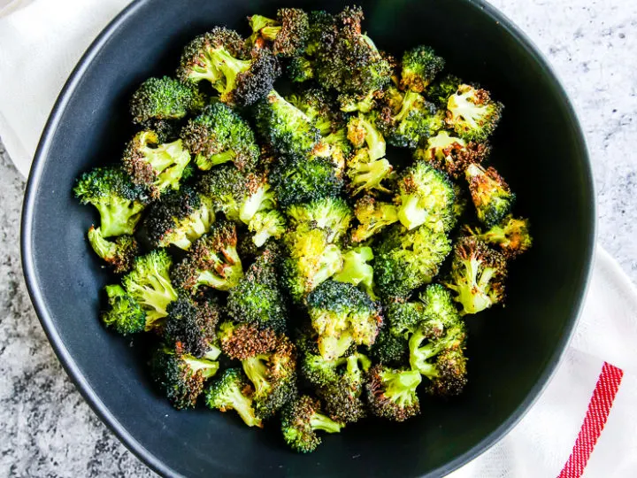 a bowl of air fryer broccoli in a black bowl on a red and white napkin