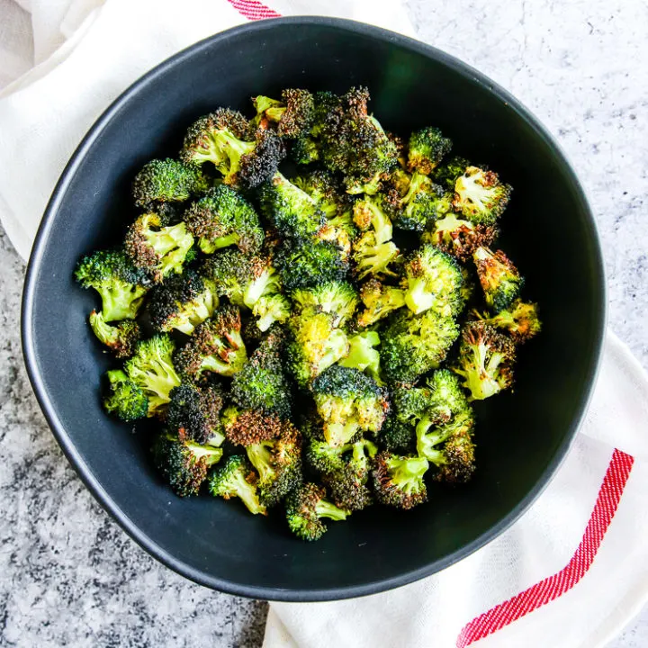 a bowl of air fryer broccoli in a black bowl on a red and white napkin