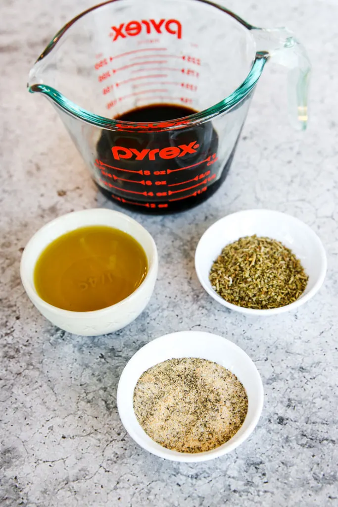 a pyrex measuring cup of balsamic vinegar, and bowls of olive oil, Italian seasonings, and salt and pepper