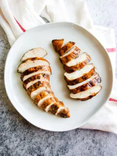 two sliced balsamic grilled chicken breasts on a white plate sitting on a white and red striped napkin