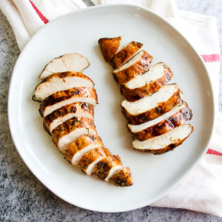 two sliced balsamic grilled chicken breasts on a white plate sitting on a white and red striped napkin