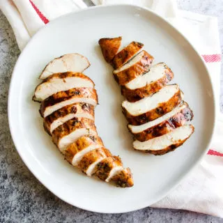 two sliced balsamic grilled chicken breasts on a white plate sitting on a white and red striped napkin