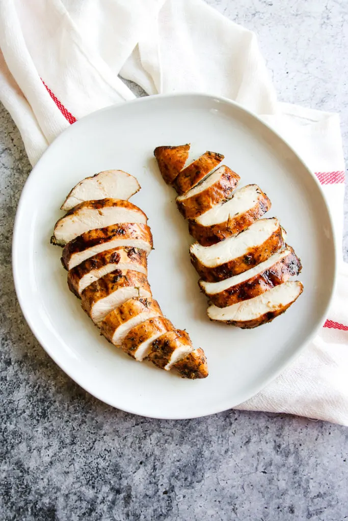 two sliced balsamic grilled chicken breasts on a white plate sitting on a white and red striped napkin