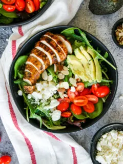 two black bowls of balsamic grilled chicken salad with feta, sliced almonds, tomatoes, and avocado