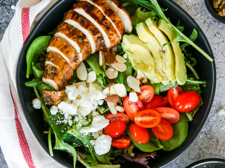 two black bowls of balsamic grilled chicken salad with feta, sliced almonds, tomatoes, and avocado