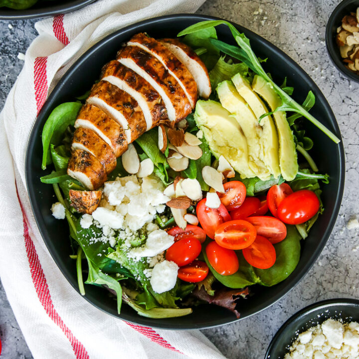 two black bowls of balsamic grilled chicken salad with feta, sliced almonds, tomatoes, and avocado