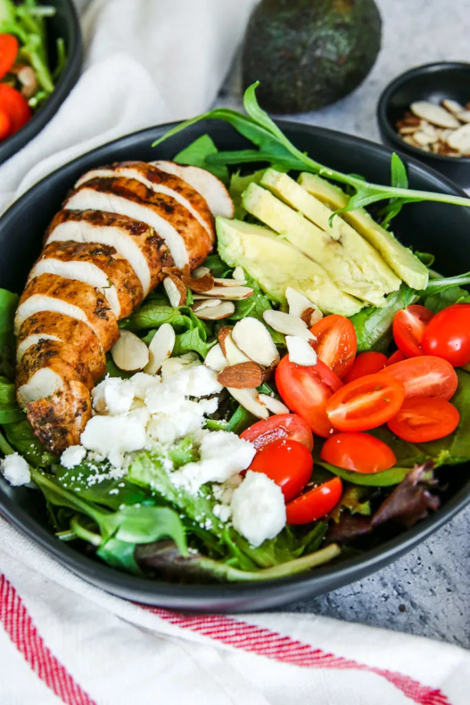 a close up of the balsamic grilled chicken salad with feta, slivered almonds, sliced cherry tomatoes, and sliced avocado