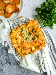 a glass baking dish full of baked buffalo cauliflower dip next to toasted bread and parsley