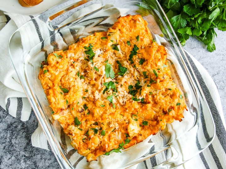 a glass baking dish full of baked buffalo cauliflower dip next to toasted bread and parsley