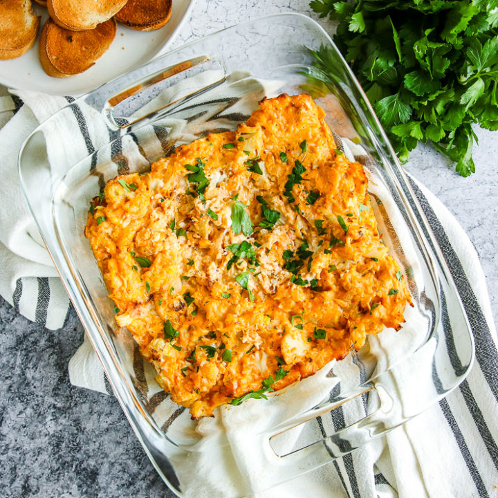 a glass baking dish full of baked buffalo cauliflower dip next to toasted bread and parsley