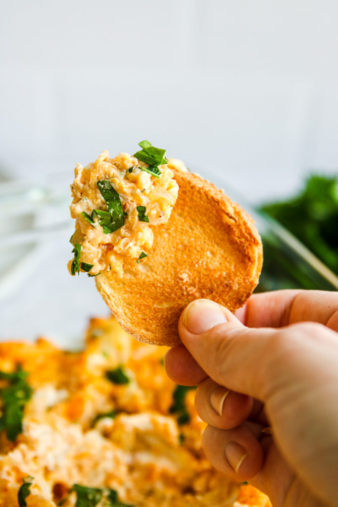 a piece of toasted bread with some buffalo cauliflower dip being held up