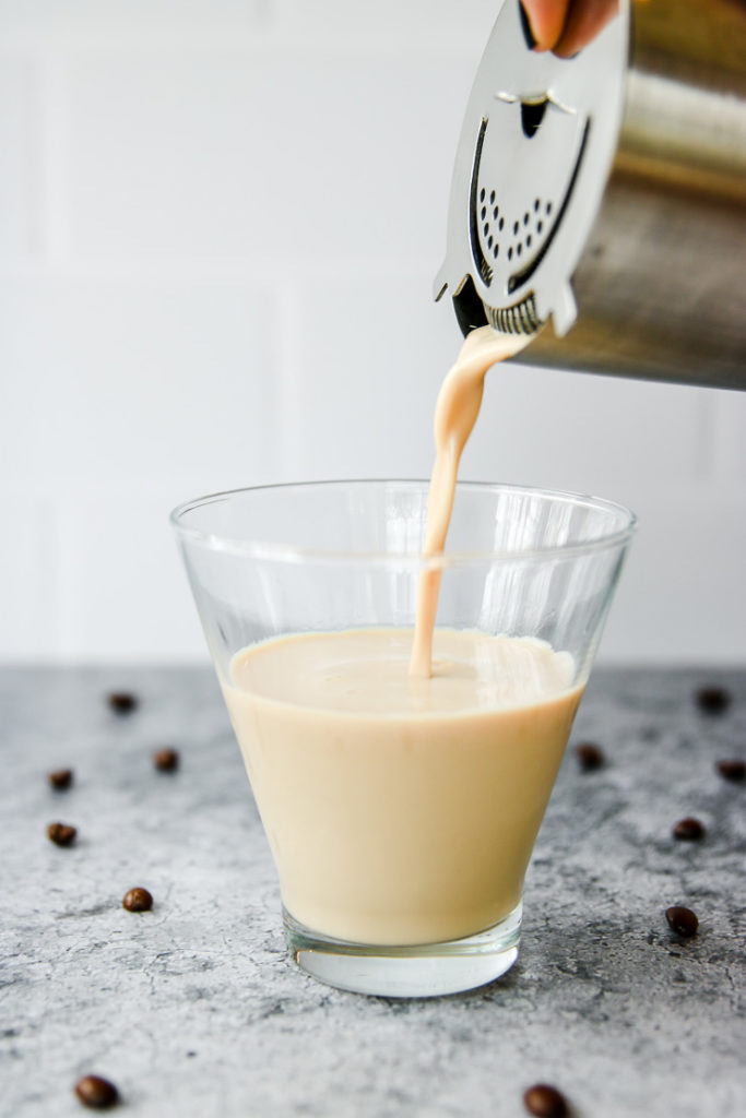 a metal strainer pouring the espresso martini into a stemless martini glass