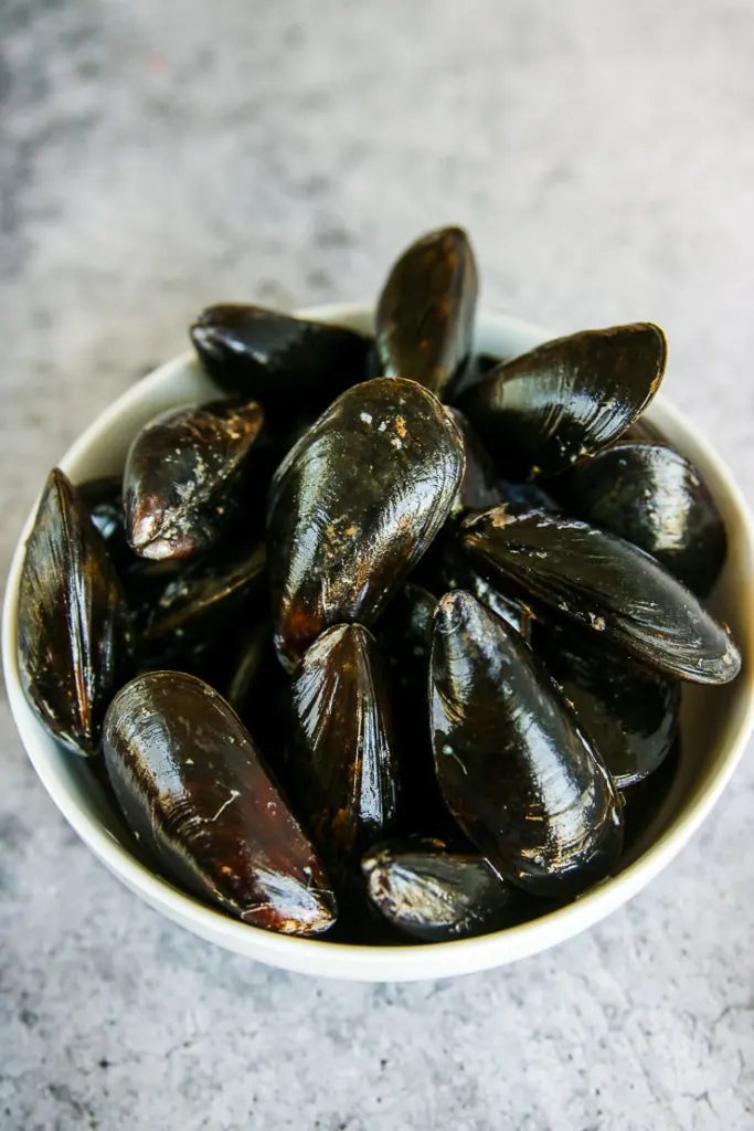 a white bowl of mussels on a grey background