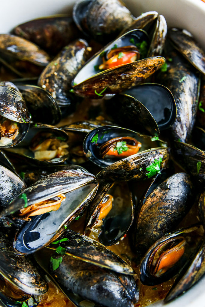 a close up of cooked garlic butter mussels sprinkled with parsley