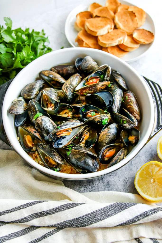 a container full of garlic butter mussels with toasted bread slices in the background