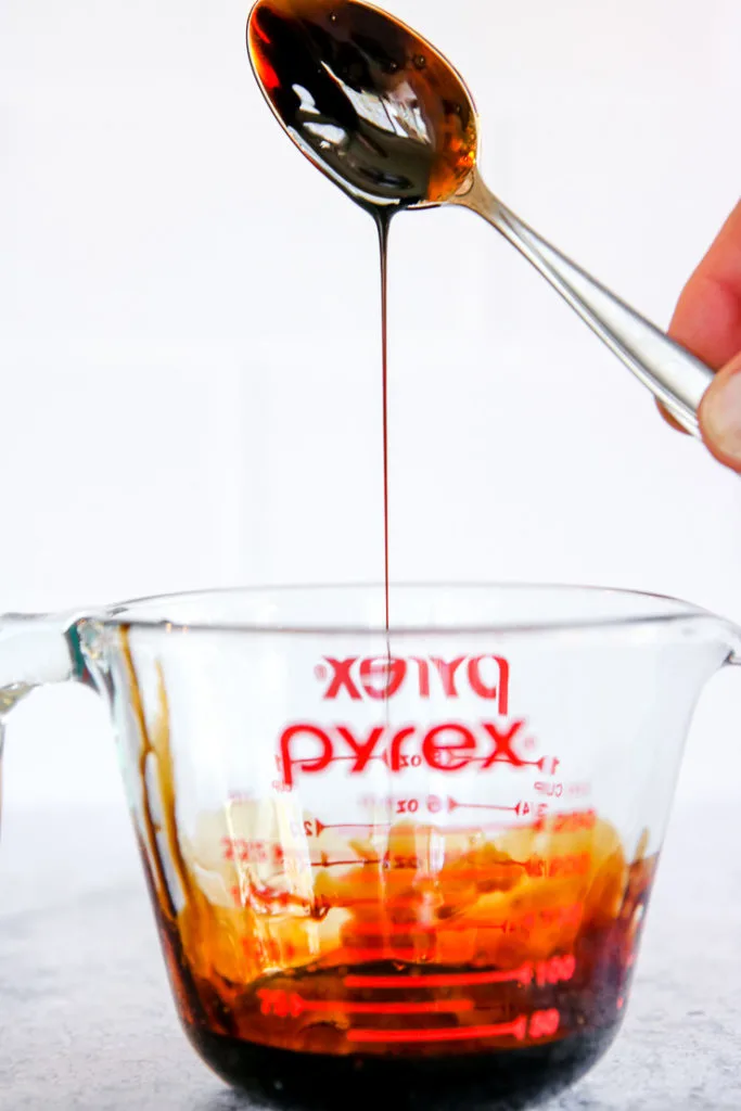 a spoon drizzling with balsamic reduction over the pyrex measuring cup