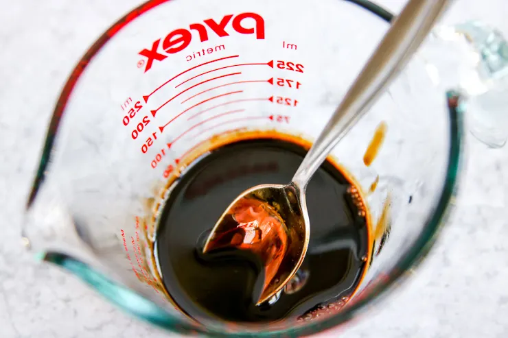 a close up of a spoon in the balsamic reduction in a pyrex measuring cup