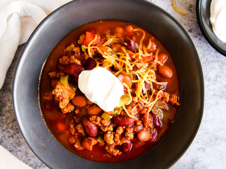 a bowl of instant pot ground turkey chili with sour cream and shredded cheese on top next to bowls of sour cream and diced jalapenos