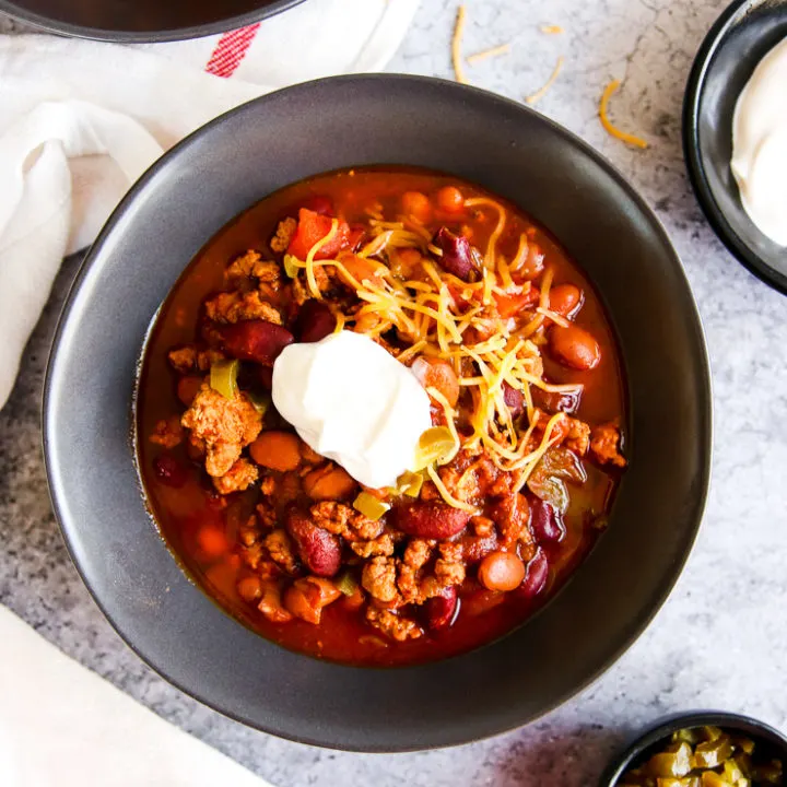 a bowl of instant pot ground turkey chili with sour cream and shredded cheese on top next to bowls of sour cream and diced jalapenos