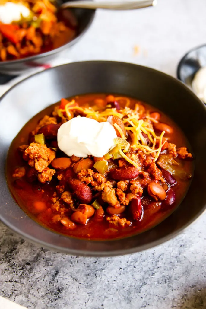 a close up of a grey bowl of instant pot ground turkey chili with a dollop of sour cream on top