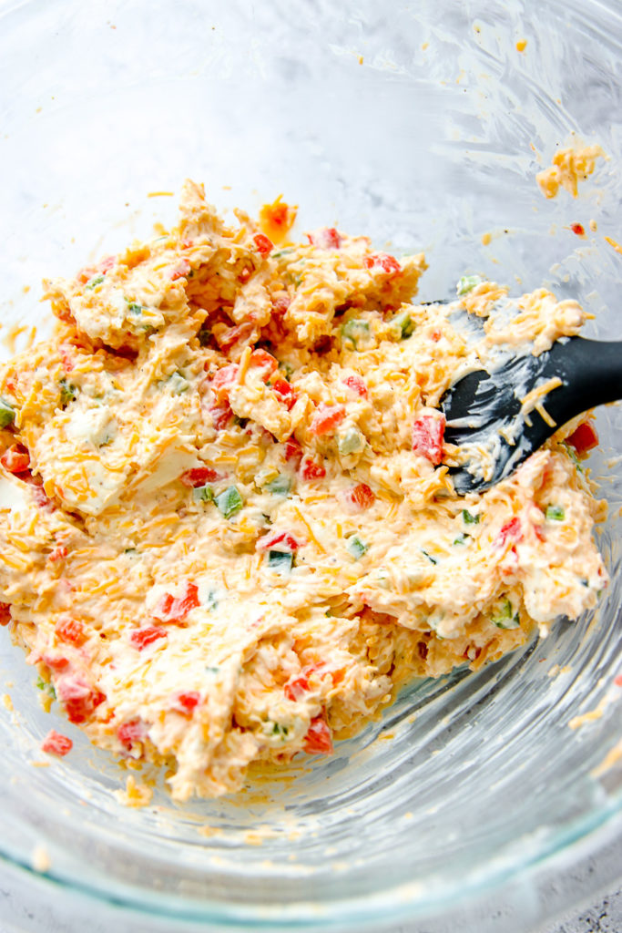 a glass bowl with a black spatula stirring the ingredients together