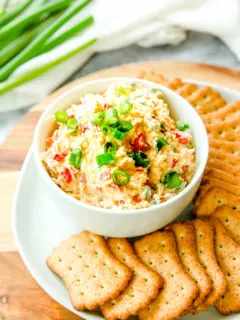 a bowl of jalapeno pimento cheese with sliced green onions on top next to crackers and full green onions