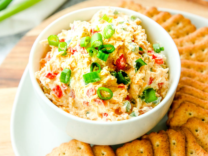 a bowl of jalapeno pimento cheese with sliced green onions on top next to crackers and full green onions