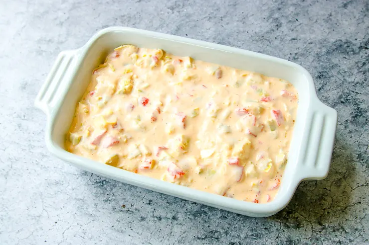 a white baking dish with roasted red pepper artichoke dip in it prior to baking