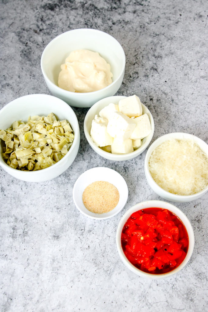 white bowls full of prepared artichokes, mayo, cream cheese, seasonings, parmesan, and roasted red peppers