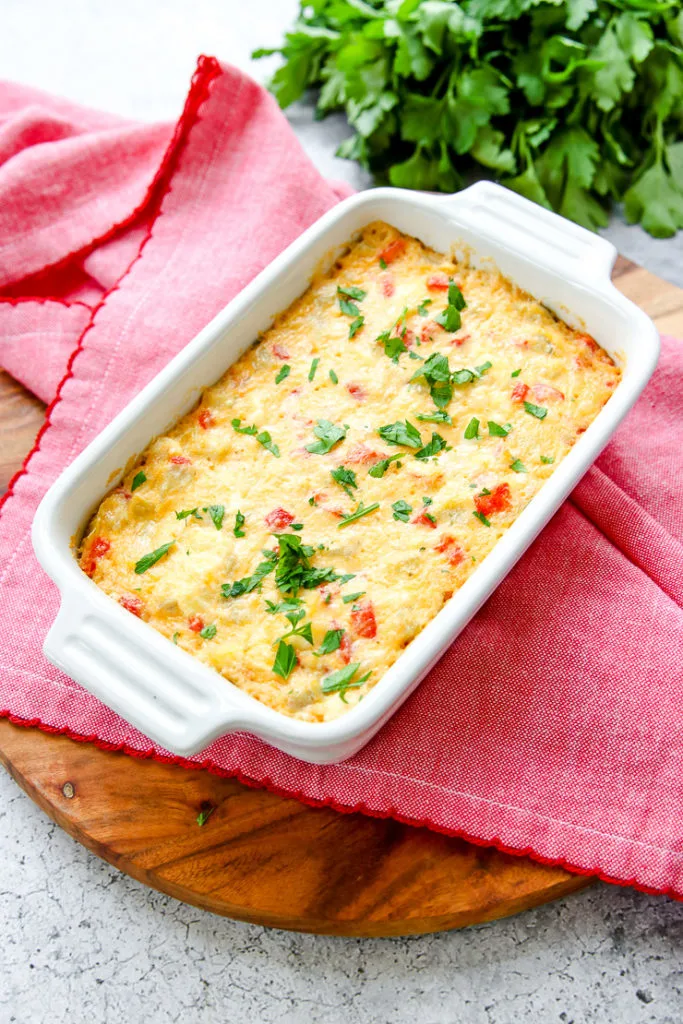 roasted red pepper artichoke dip on a red napkin on a wooden round cutting board with parsley in the background