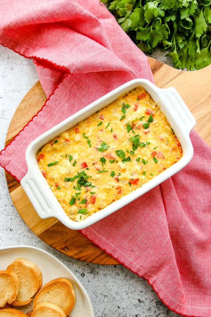 an overhead shot of the roasted red pepper artichoke dip on a red napkin on a round cutting board