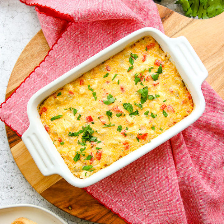 an overhead shot of the roasted red pepper artichoke dip on a red napkin on a round cutting board