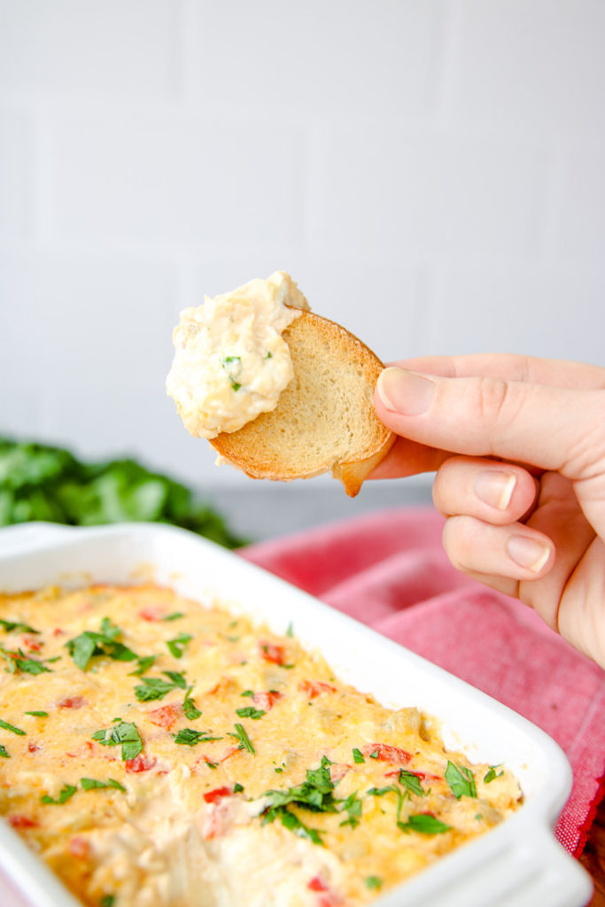 a toasted piece of bread being held up with roasted red pepper artichoke dip on it