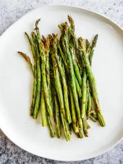 a white plate full of asparagus right from the air fryer