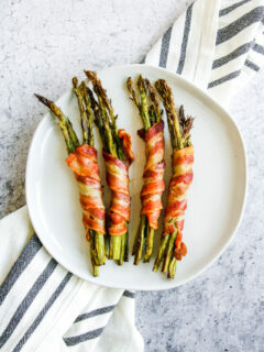 a plate of air fryer bacon wrapped asparagus on a grey and white napkin