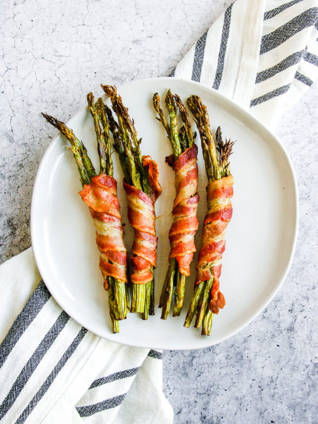 a plate of air fryer bacon wrapped asparagus on a grey and white napkin