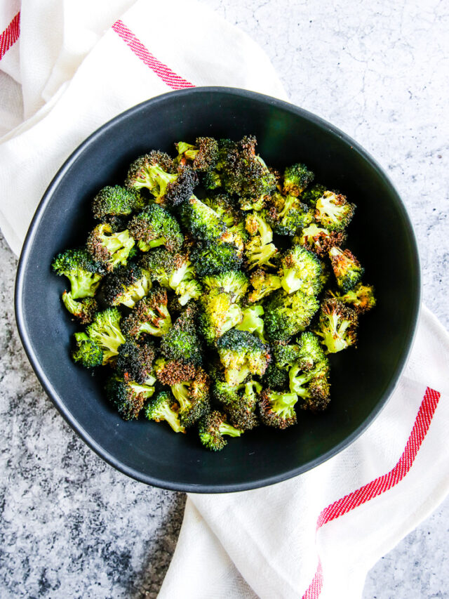 a bowl of air fryer broccoli in a black bowl on a red and white napkin