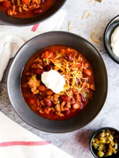 a bowl of instant pot ground turkey chili with sour cream and shredded cheese on top next to bowls of sour cream and diced jalapenos