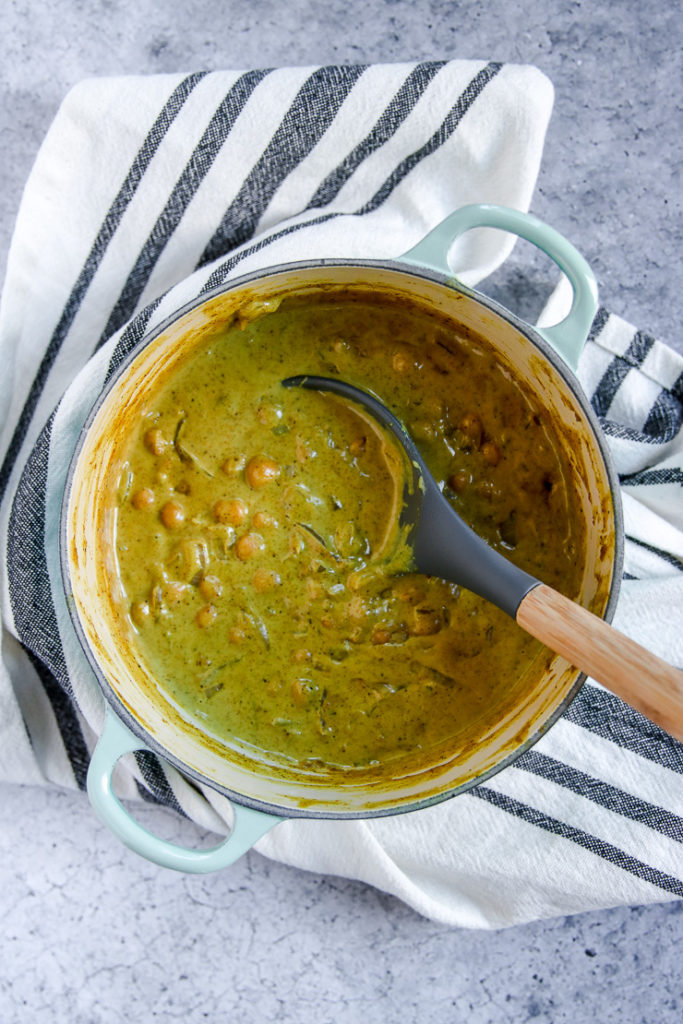 a blue sauce pan full of chickpea coconut curry on a striped napkin