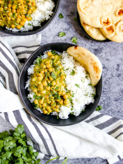 two black bowls full of rice, naan, and chickpea coconut curry