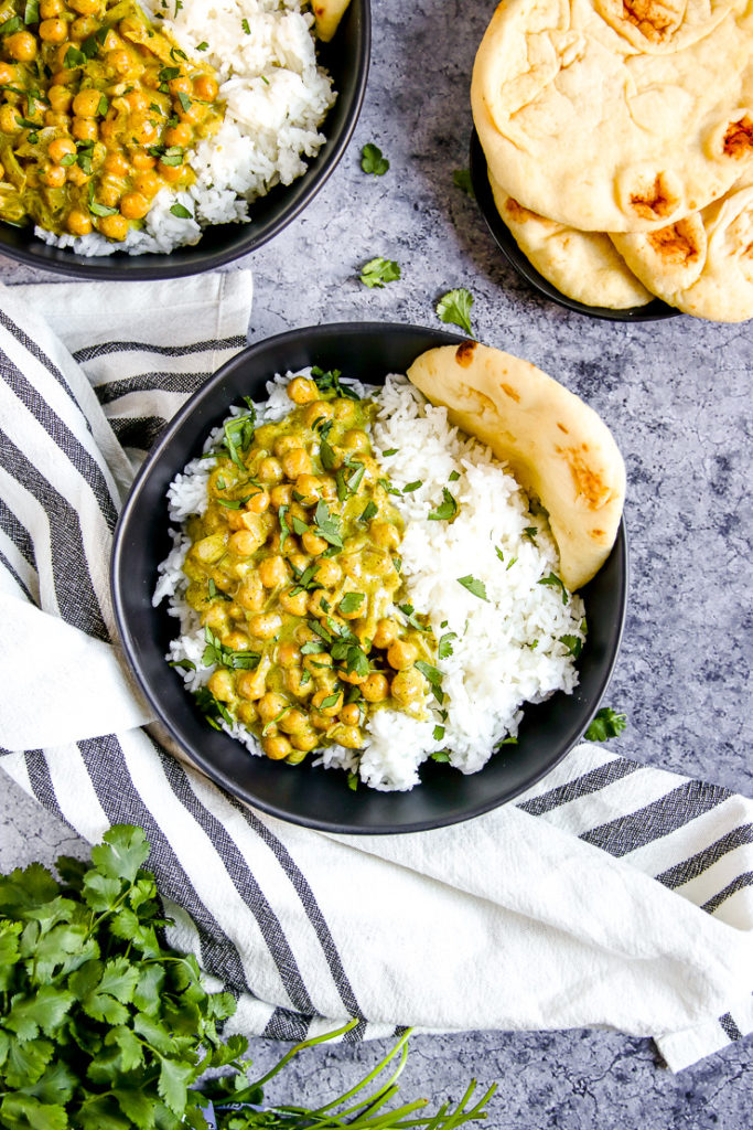 two black bowls full of rice, naan, and chickpea coconut curry