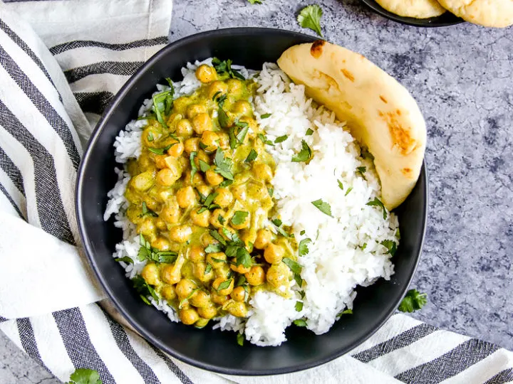 two black bowls full of rice, naan, and chickpea coconut curry