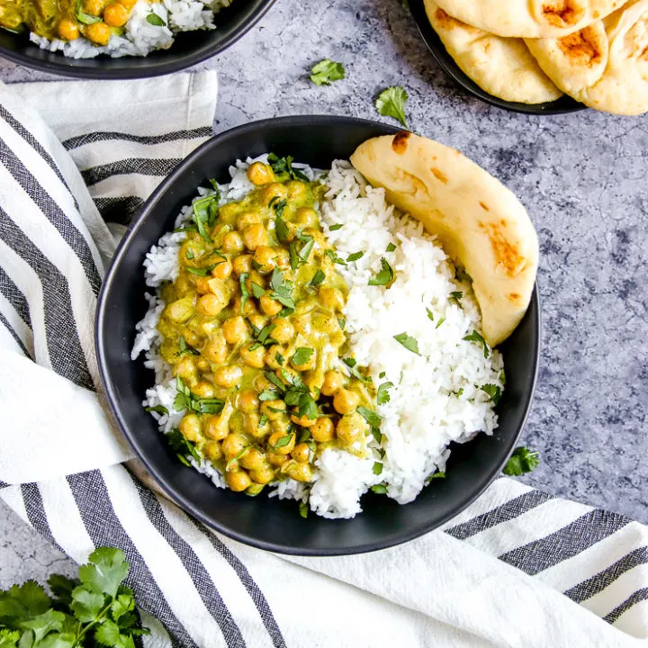 two black bowls full of rice, naan, and chickpea coconut curry