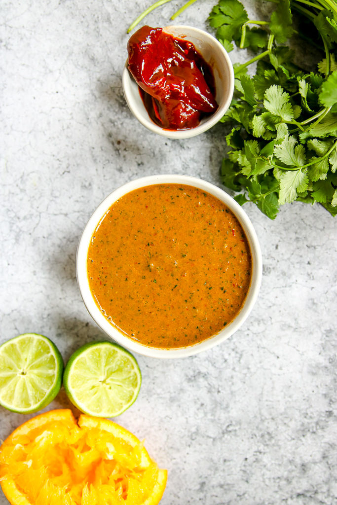 a bowl of chipotle lime sauce with an juiced orange and lime, chipotles, and cilantro next to it