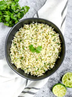 a black bowl on a striped napkin with cilantro lime cauliflower rice in it