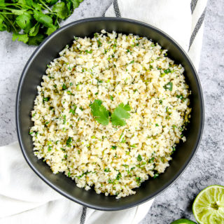 a black bowl on a striped napkin with cilantro lime cauliflower rice in it