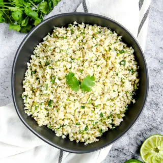 a black bowl on a striped napkin with cilantro lime cauliflower rice in it